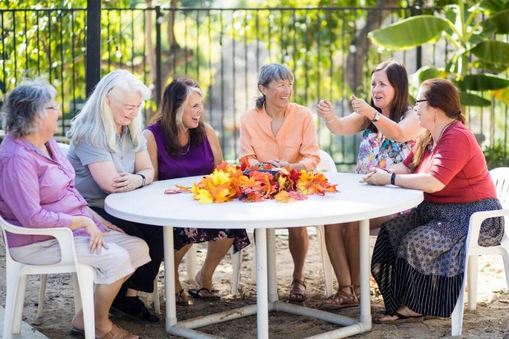 a group of size middle aged female friends sitting at a table laughing and talking to show how to improve social wellness