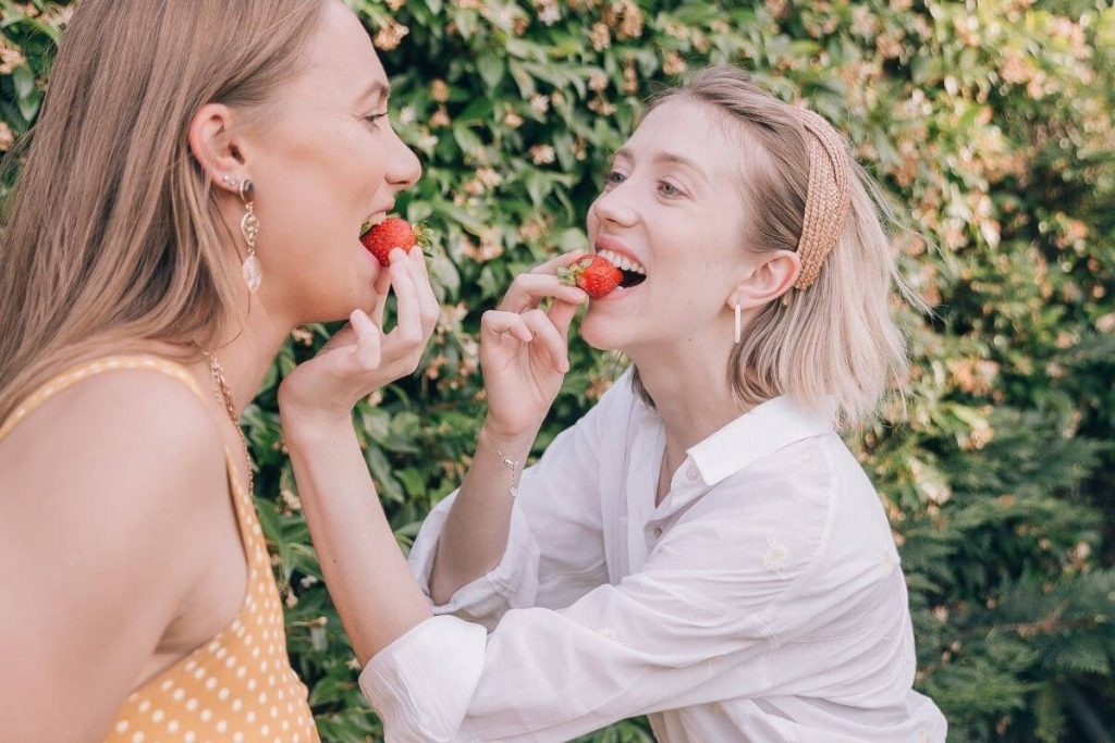 two happy friends feeding each other strawberries