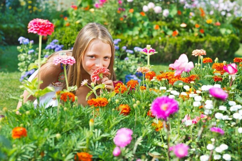 a young girl bends down to smell wild flowers in a field