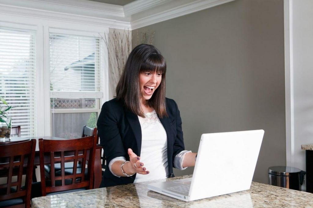 woman wearing a white blouse and black blazer excitedly looks at her laptop as she watches a LIVE presentation of trendy boutique clothes women love