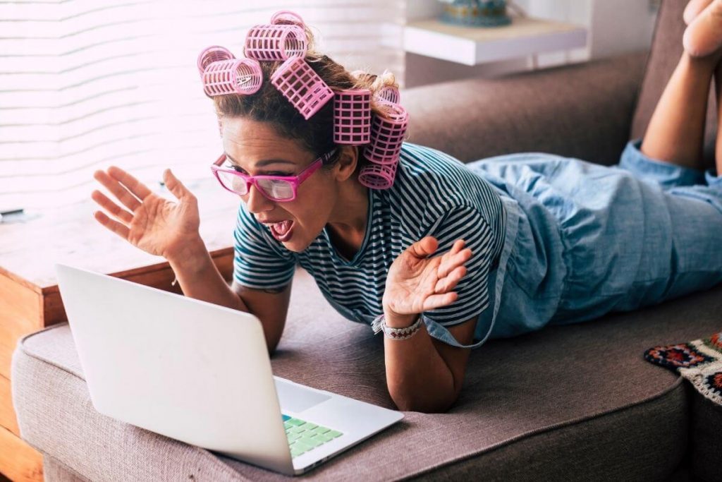 casually dressed woman with huge curlers in her hair is excited as she watches a LIVE presentation on her laptop about trendy online boutique clothes women love