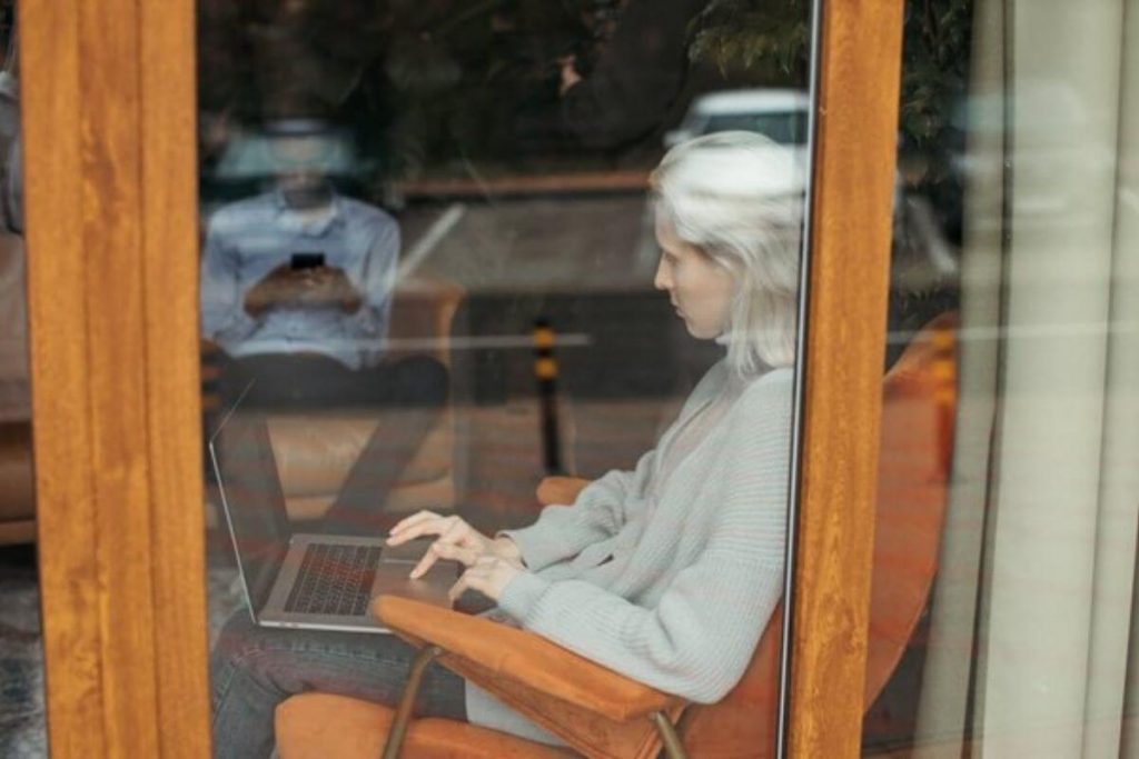 a woman works on her laptop as she sits in a chair next to a window