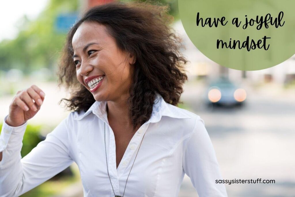 a dark skinned very happy woman walks down the stress with a big smile on her face and a note that says have a joyful mindset