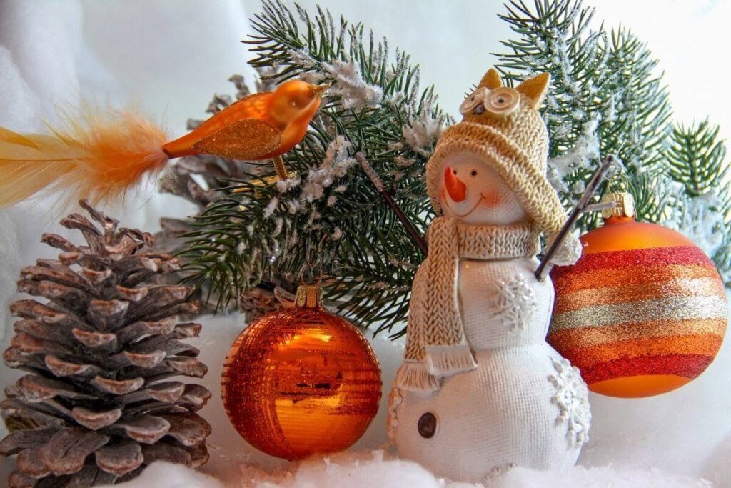 pinecone orange bird orange 2 christmas tree ornaments greenery snow and a fabric snowman with an owl cap on his head showing how to get in the christmas spirit