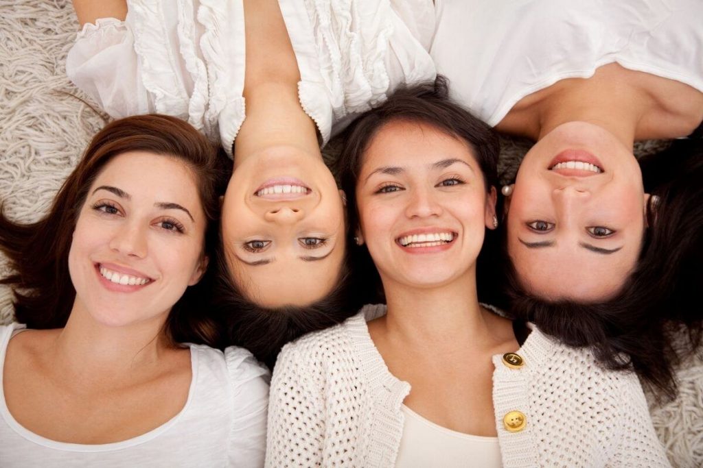 four confident and smiling women laying on the floor with their heads together facing alternate directions