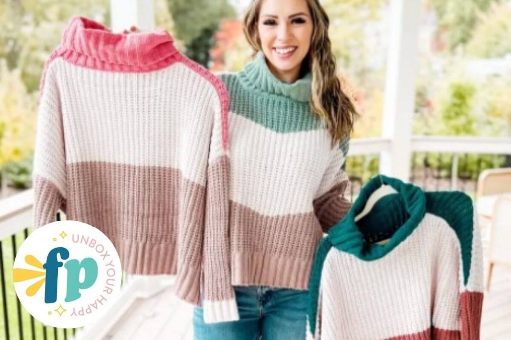 a beautiful young model wears a tri-tone fall sweater and holds up two other sweaters in different colors that are sold by freckled poppy boutique