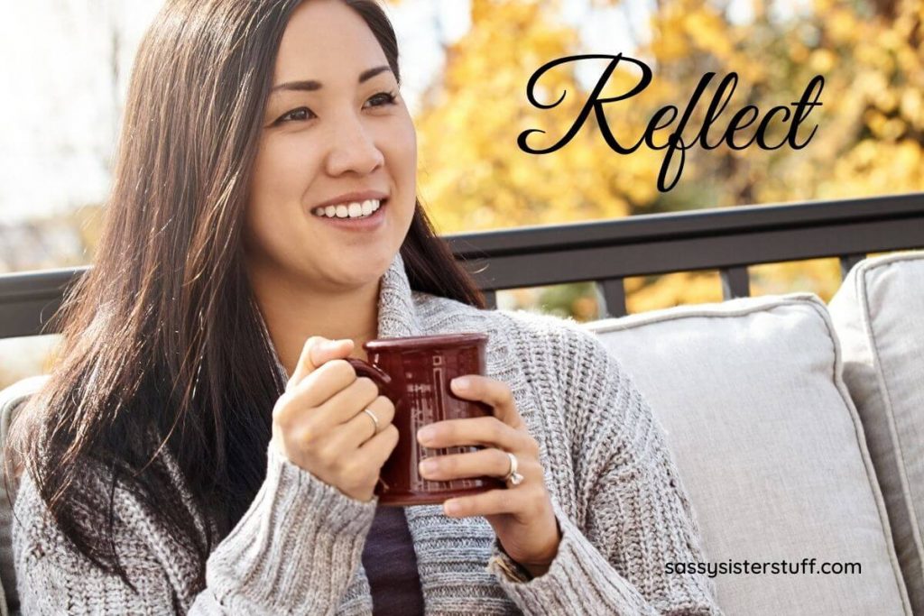 a beautiful woman sits outside on a porch in the fall wearing a cozy sweater drinking a cup of chocolate and reflecting on her health mindset