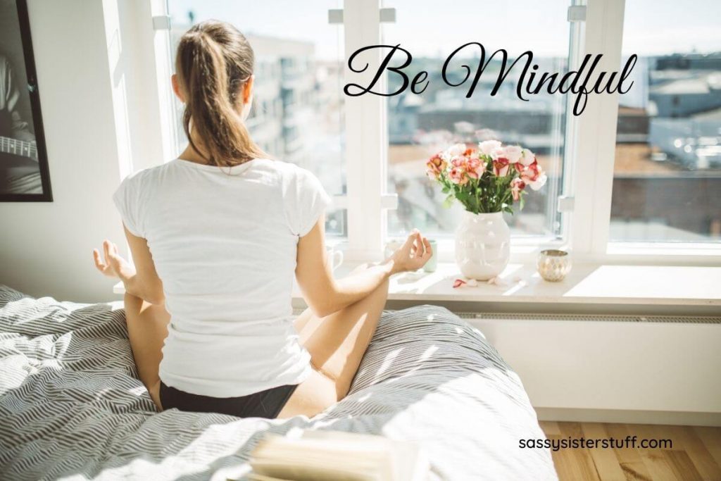 a woman sits on a bed looking out a big window doing yoga and working on developing a healthy mindset