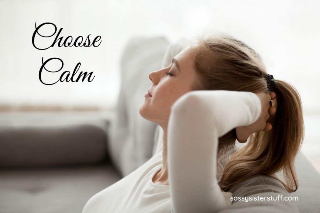 a women sits on a sofa with her hands clasped behind her head relaxing with her eyes closes choosing to be calm and have a healthy mindset