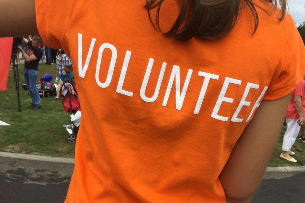 a woman wears an orange tee shirt with the word volunteer on the back