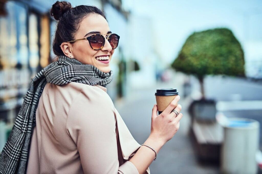 happy business woman holds a coffee and walks down the stress with a scarf around her neck showing how to live your best life