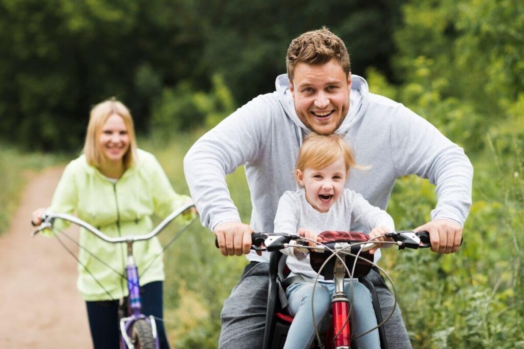 a happy young mom and dad take a little girl on a bike ride on a path through the woods