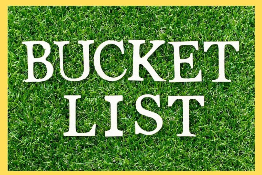 white wooden letters spell out bucket list on a grassy background with a yellow border