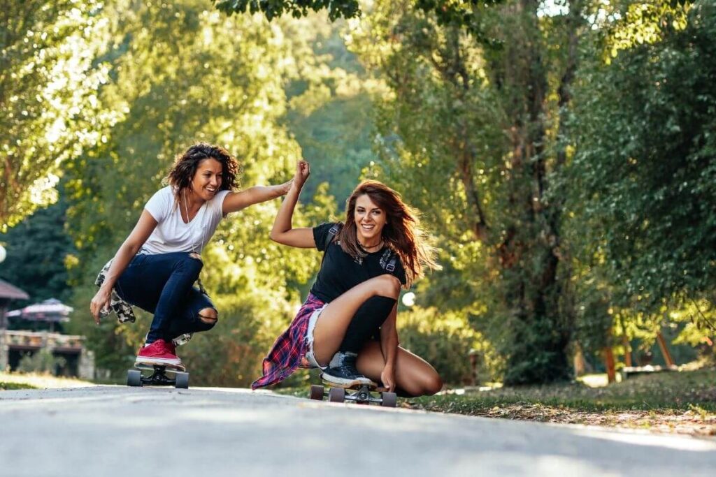 two women have fun skateboarding down a wooded street