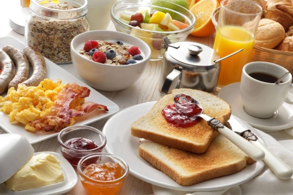 a delicious breakfast with eggs bacon sausage toast jelly orange juice coffee fruit rolls oats and butter