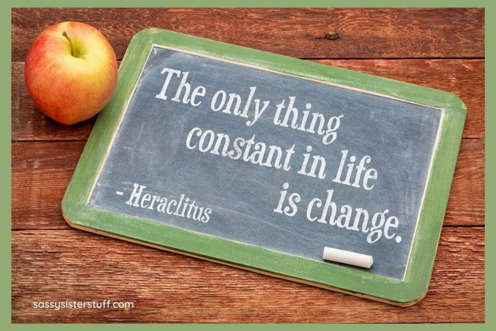 a chalkboard with a green border laying on a wooden table next to an apple and a quote that says the only thing constant in life is change