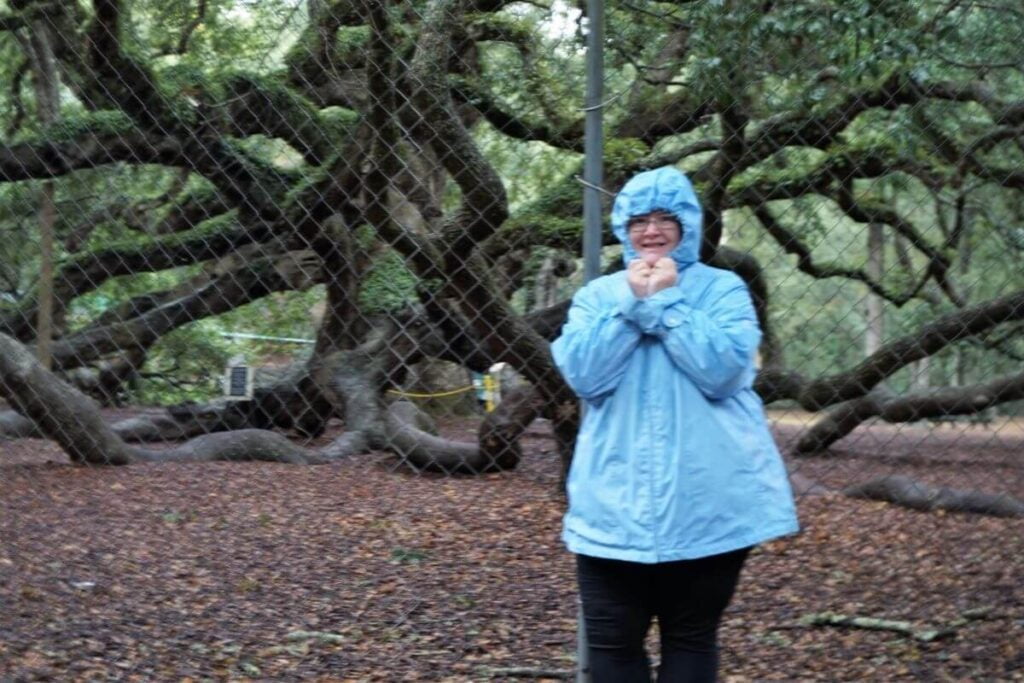 woman in a blue rain coat stands in front of the angel oak tree on a weekend in charleston sc