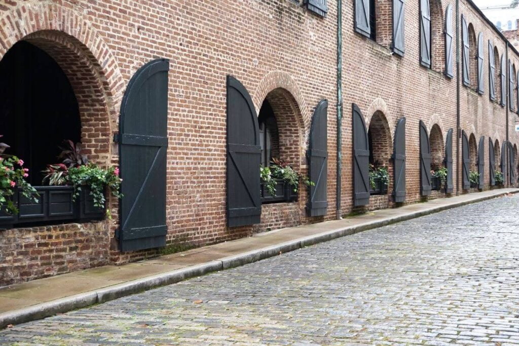 a beautiful cobblestone street and a brick building with flower boxes and window shutters that look like barn doors