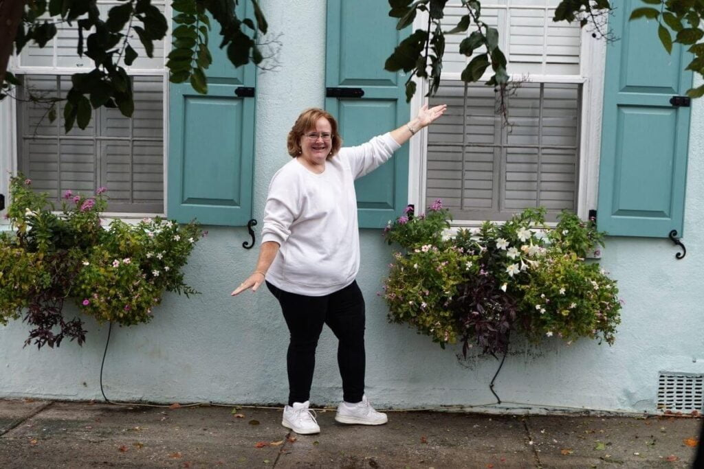 a happy woman standing in front of a green house on rainbow row on a weekend in charleston sc