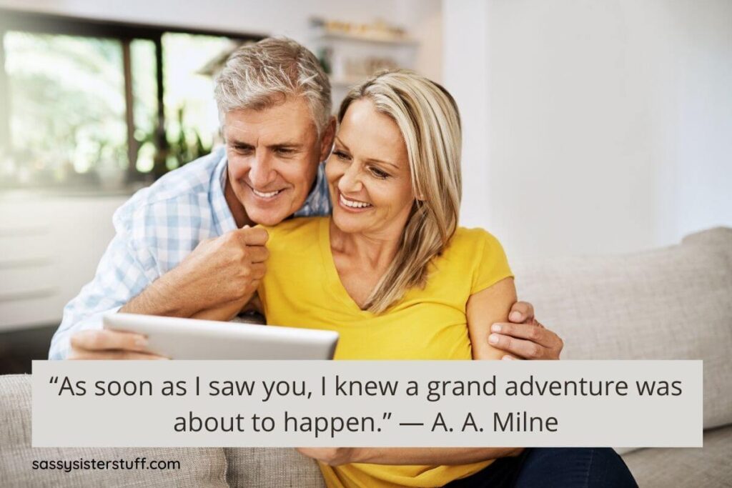 a happy middle-aged man and woman sit together on a sofa planning their next adventure on a laptop