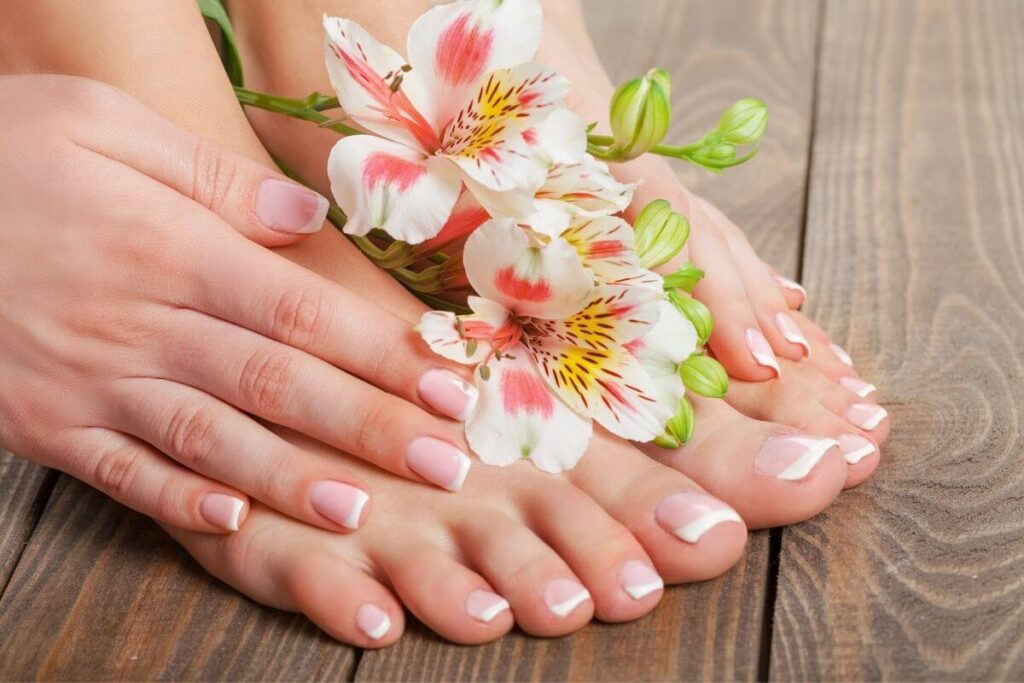 nealty manicured toes and fingers done in light pink with white tips and pink flowers laying on top of the hands and feet