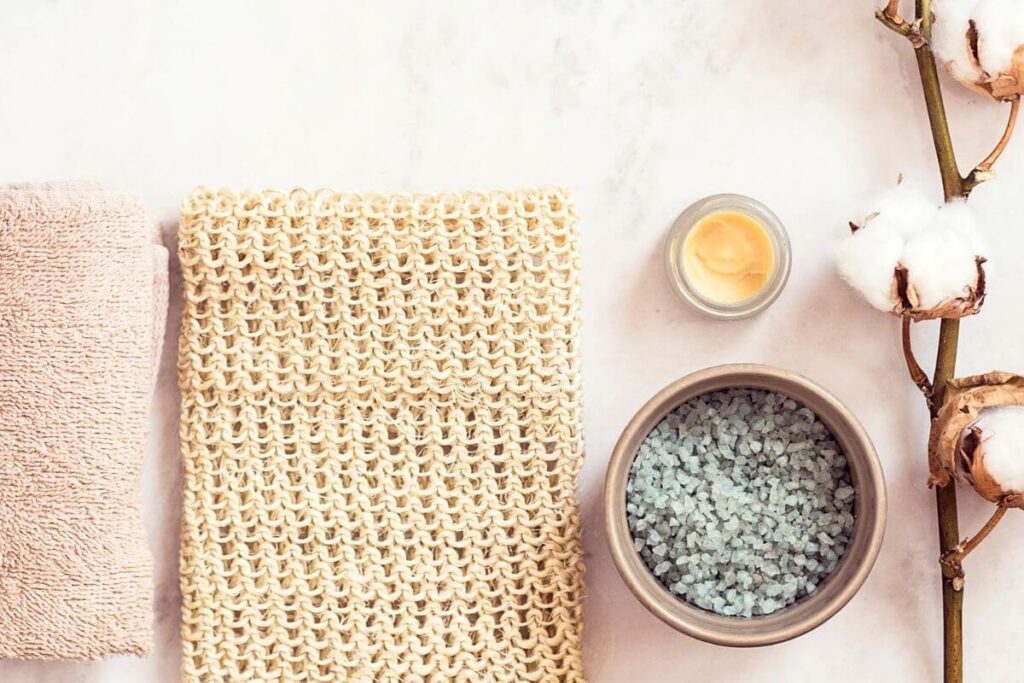 crystals minerals raw cotton loofa and a cotton towel lay on a pink marble counter for a self-care challenge