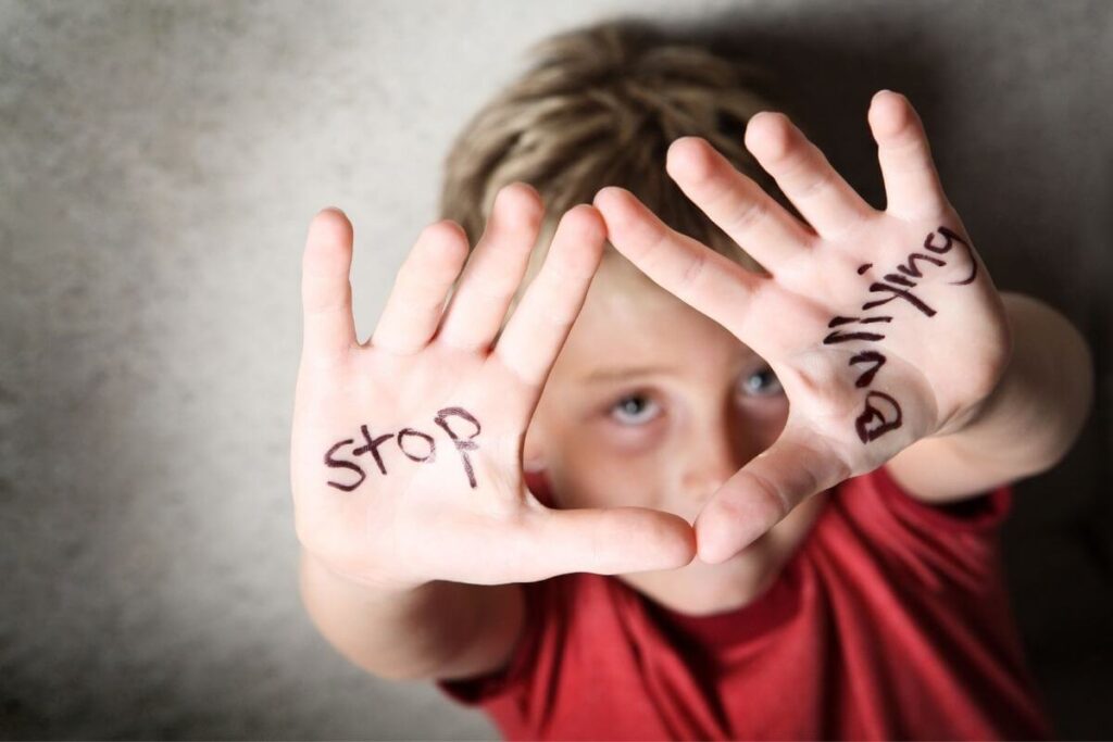 a young boy in a red shirt holds his hands up to show he has written stop bullying on the palms of his hands