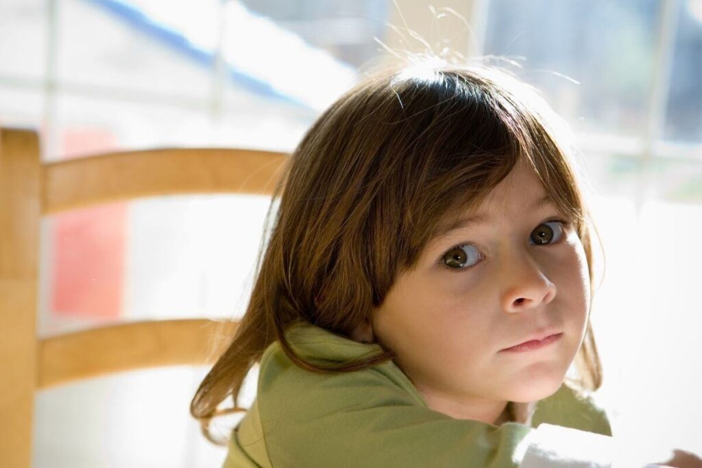 young girl sits in a school chair looking blankly into space as she feels lonely and isolated