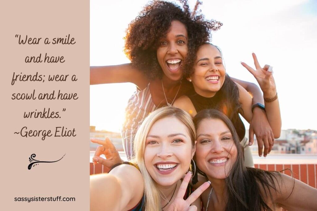 four happy young women smiling with their heads together and showing peace signs with a smile quote by george eliot