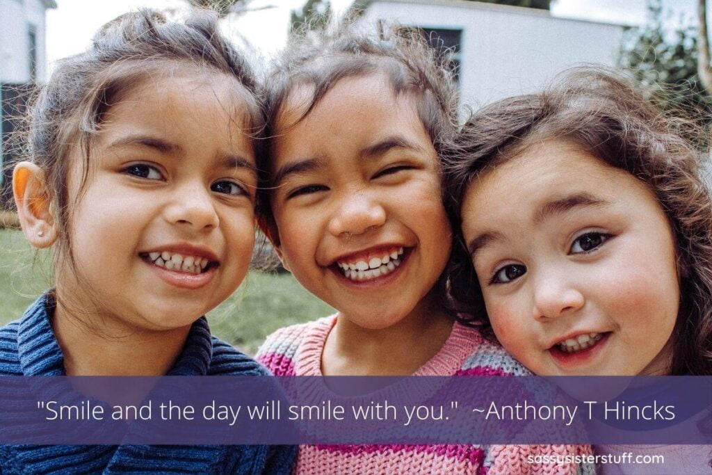 three adorable little girls with their heads together smiling big and a smile quote