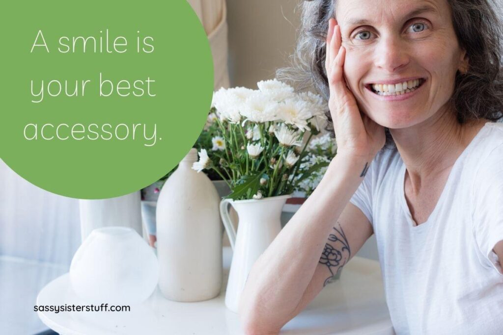 a middle aged woman smiles beautifully at the camera with a vase of white flowers next to her and a smile quote encouraging you to smile