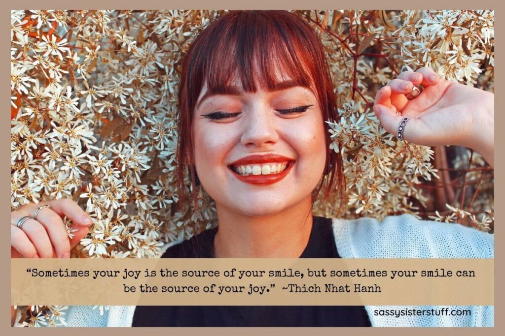 a beautiful red haired woman laying in white flowers smiling with her eyes closed and a smile quote to encourage you to smile more