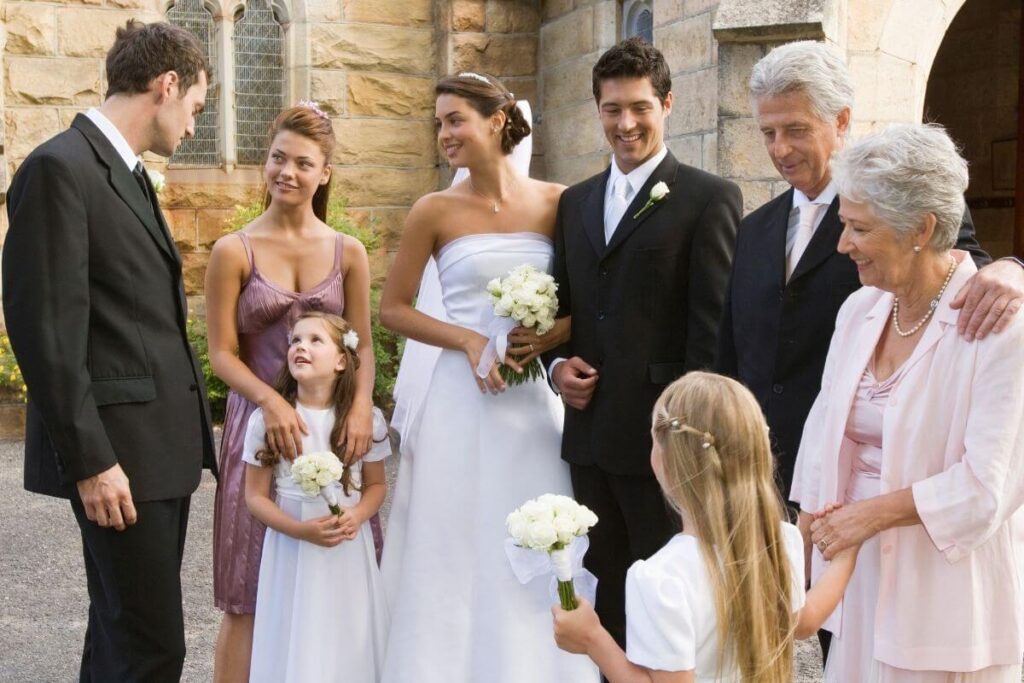 four generations of family gather dressed up for a wedding stand outside a church with a bride and groom