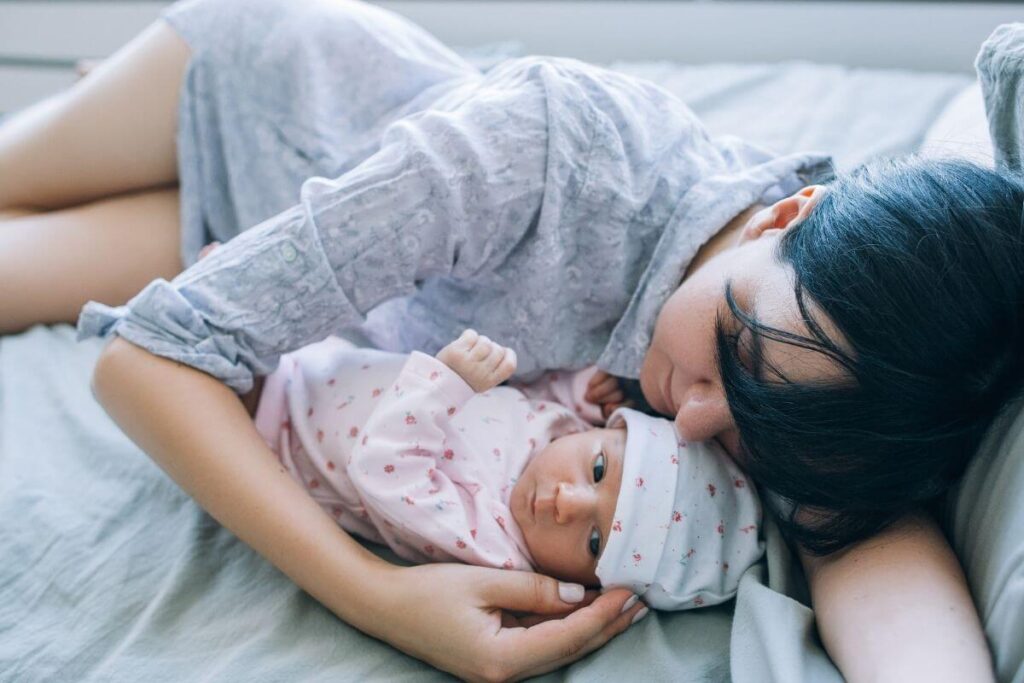 a young mother lays with her infant daughter because the baby has been awake all night and the mom is tired