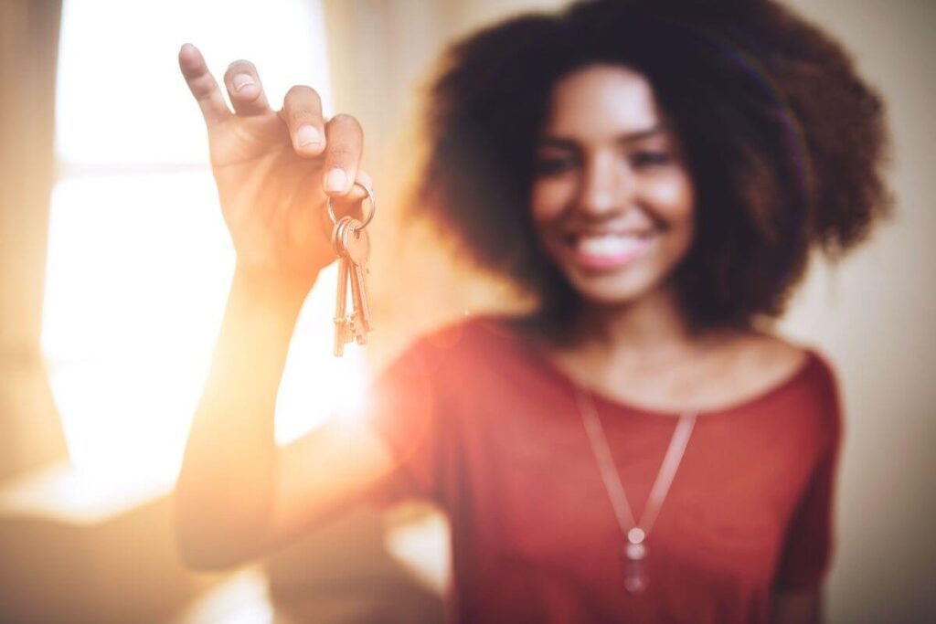 a dark skinned pretty woman wearing a red dress holds a set of keys up to turn them into her landlord because every journey begins with a choice and she has chosen to move to a new home for a new beginning