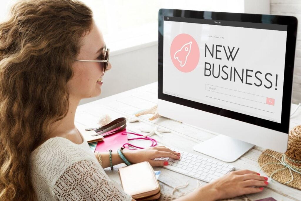 a happy young woman sits at her new at home computer desk and works on her new business on her computer because she has been inspired by quotes about new beginnings to start her own business