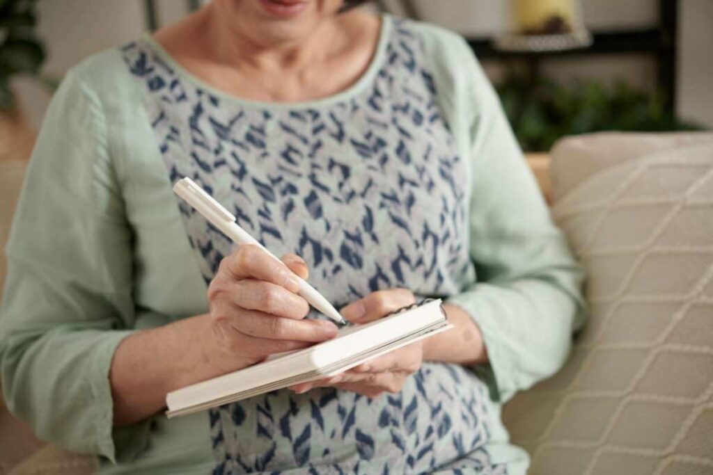 a close up of a middle aged woman using her gratitude journal prompts to write in her journal or diary