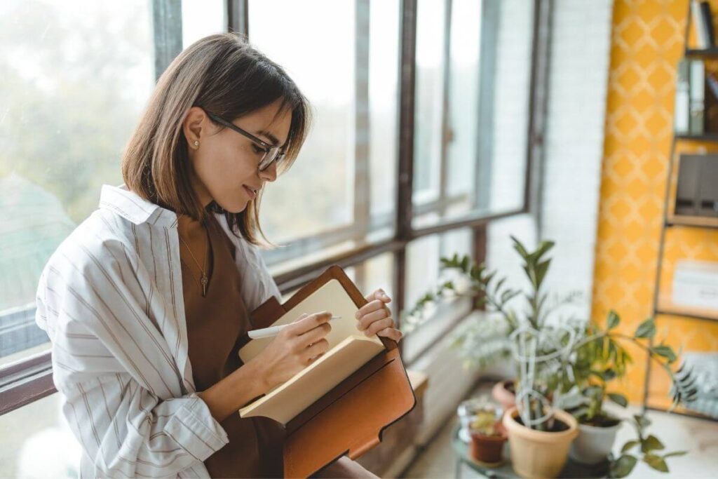 a woman uses journal prompts to write in a journal in her office