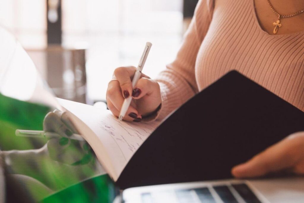 a close up image of a woman wearing a peach sweater writing in her journal