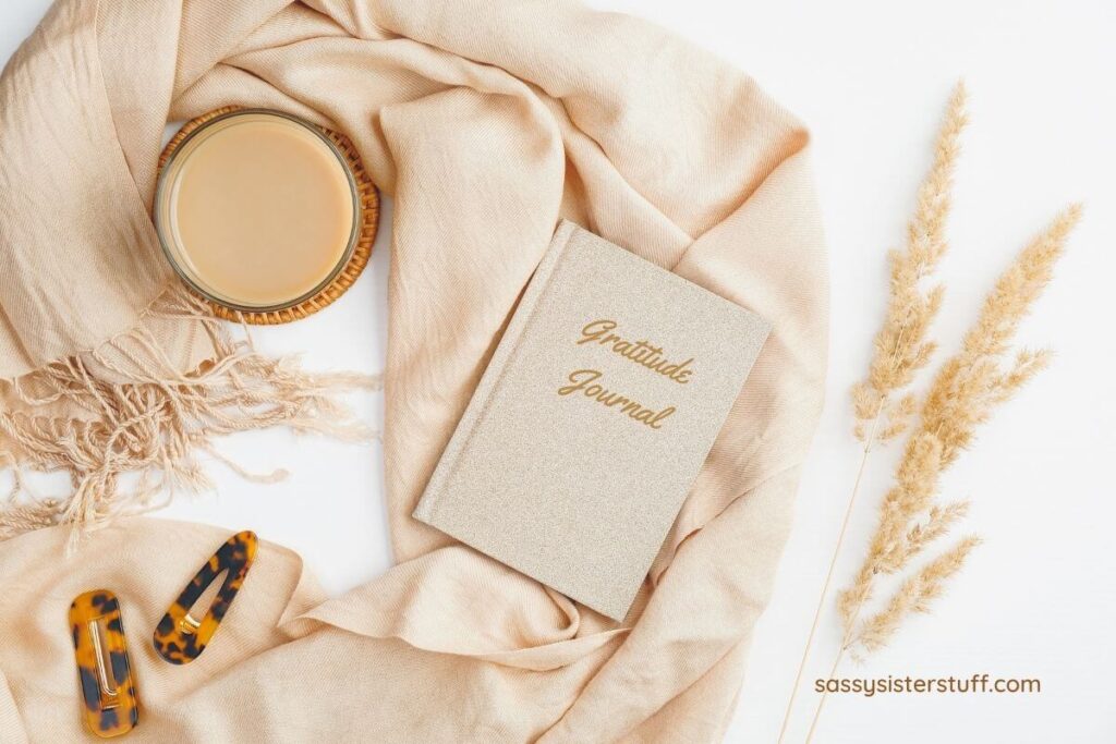 a beige and white image of a woman's scarf hair barrettes a candle and a gratitude journal