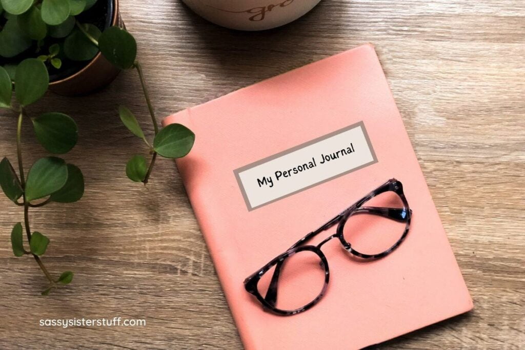 a wood grain table with a green potted plant and a peach colored journal with glasses laying on top