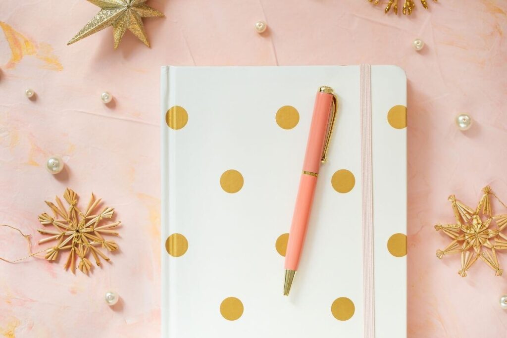 a beautiful white journal with gold dots sits on a peach background that has pearls and gold stars on it and a peach colored pen