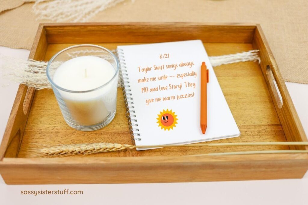 a wooden tray with a white candle and a spiral notebook with a journal entry and an orange pen sitting on the tray