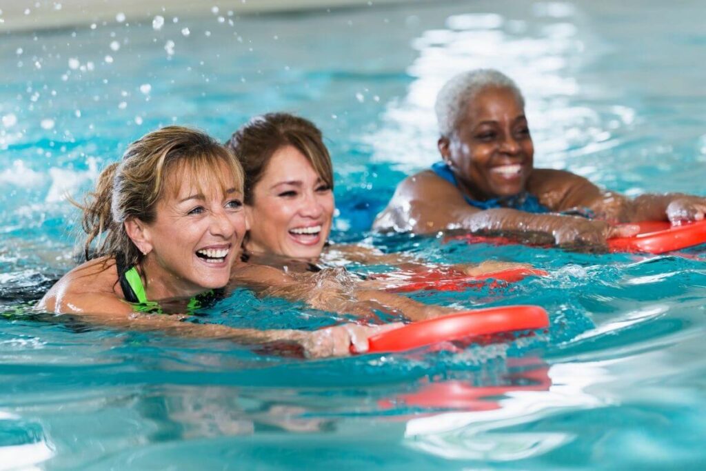 three happy women of varying ages take an aqua exercise class at an indoor pool to help make today a great day