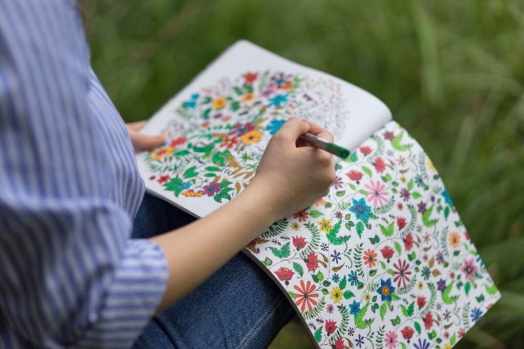 top view of woman coloring calming coloring pages outside as she sits in the grass and relaxes