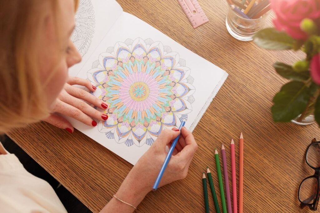 top view of woman sitting at a desk coloring a mandala calming coloring page with pastel pencils