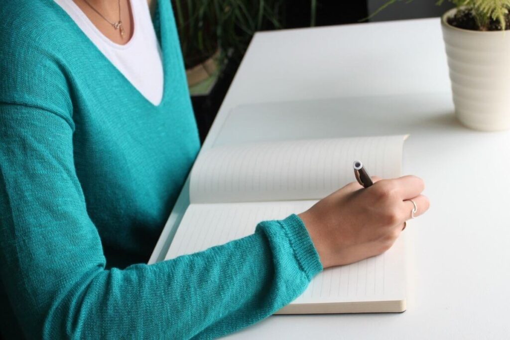 top view of a woman starting to use journaling prompts for healing at a desk with a plant overlooking a large window