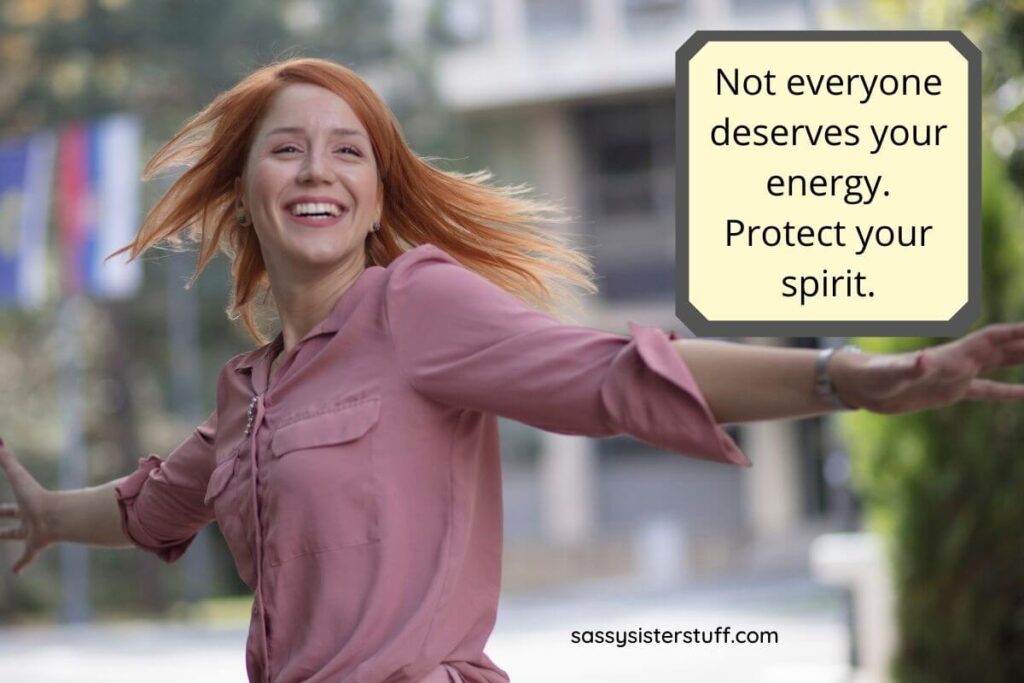 a cheerful red haired woman swings her arms around in a circle on the street plus an inspirational quote about protecting your energy and spirit