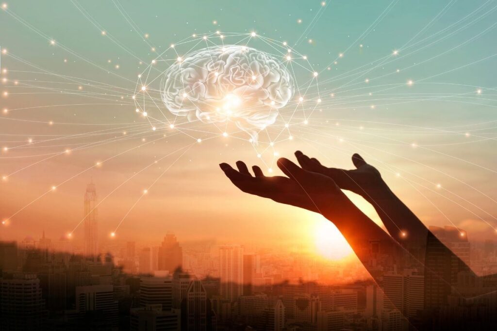 a green and orange sky background with hands holding up a model of a brain that is absorbing things from all over the world to represent that you can rewire your anxious brain