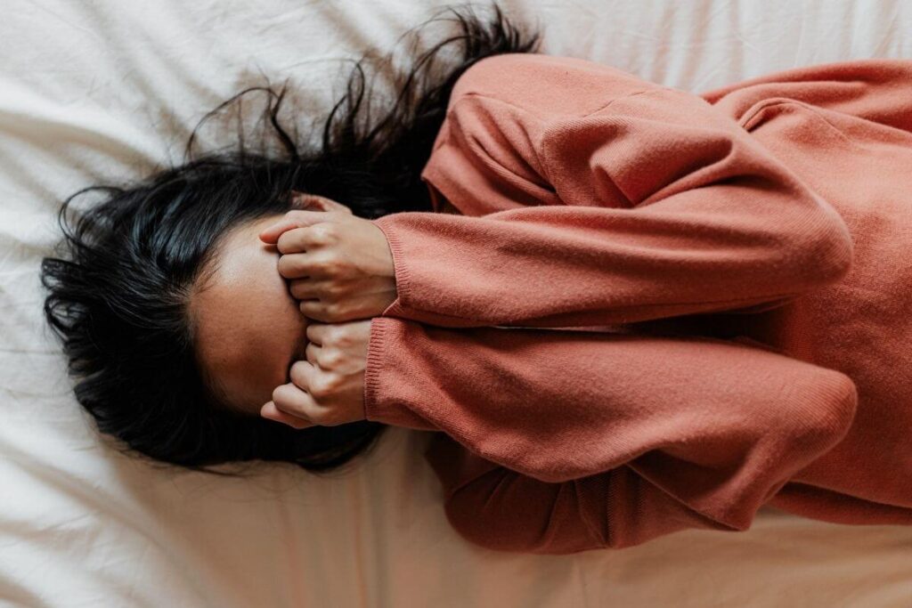 a young woman lays on a bed with her hands covering her eyes appears to be frustrated by all that is going through her brain